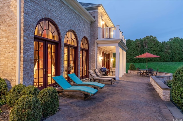 patio terrace at dusk featuring a balcony and french doors