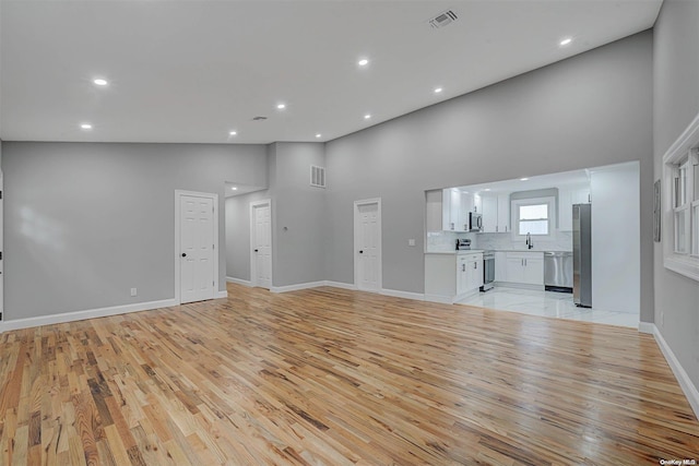 unfurnished living room featuring light wood-type flooring, sink, and high vaulted ceiling