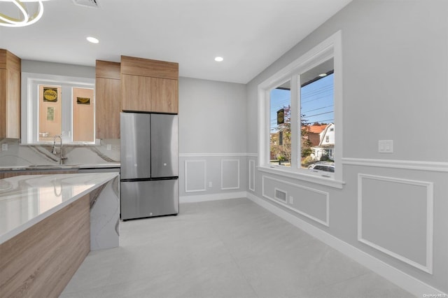 kitchen with light stone countertops, decorative backsplash, sink, light brown cabinets, and stainless steel refrigerator