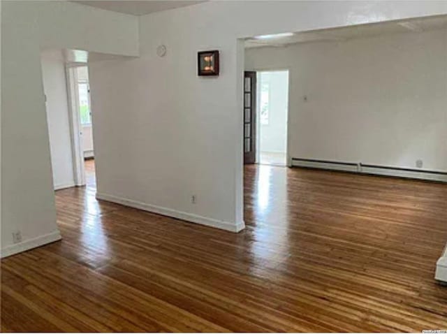 empty room featuring baseboard heating and dark wood-type flooring