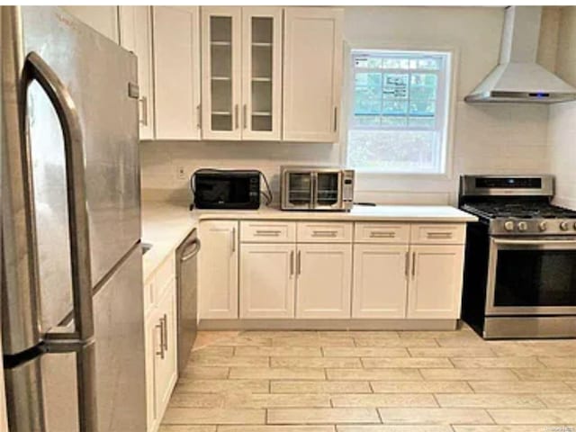 kitchen featuring wall chimney exhaust hood, stainless steel appliances, light hardwood / wood-style flooring, backsplash, and white cabinets