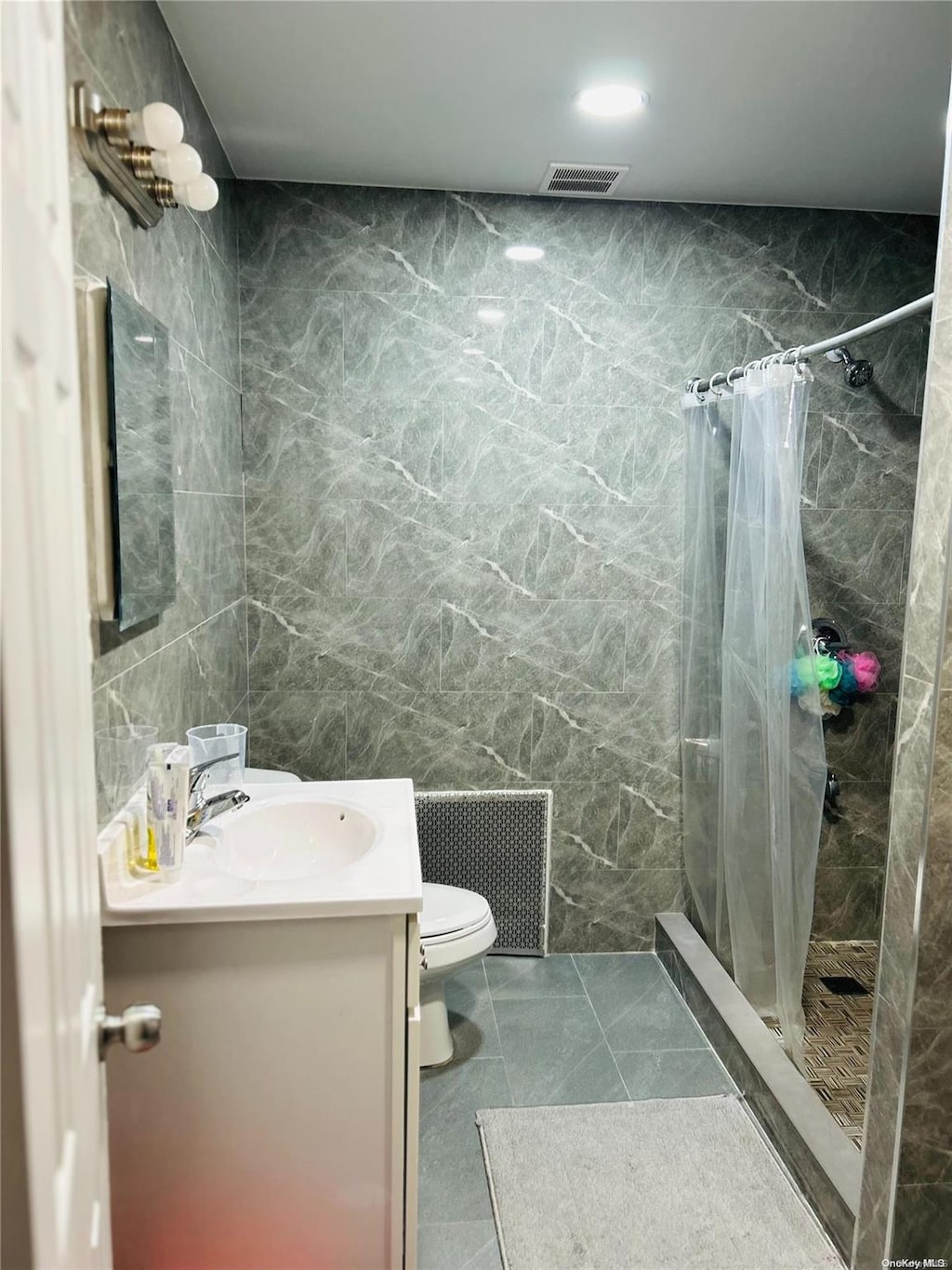 bathroom with toilet, vanity, tile walls, and walk in shower