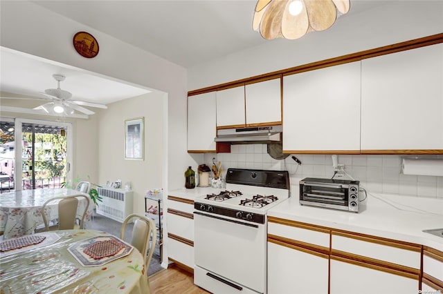 kitchen with white gas range, ceiling fan, light hardwood / wood-style flooring, decorative backsplash, and white cabinets