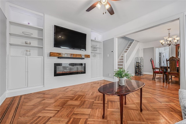 living room with built in features, a fireplace, parquet floors, and ceiling fan with notable chandelier