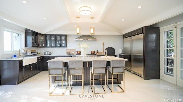 kitchen featuring sink, extractor fan, vaulted ceiling, decorative light fixtures, and a kitchen island with sink