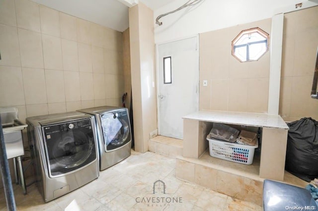 clothes washing area with washing machine and dryer and tile walls