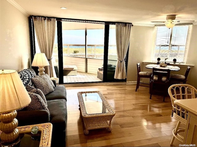 living room featuring ceiling fan, a water view, ornamental molding, and light wood-type flooring