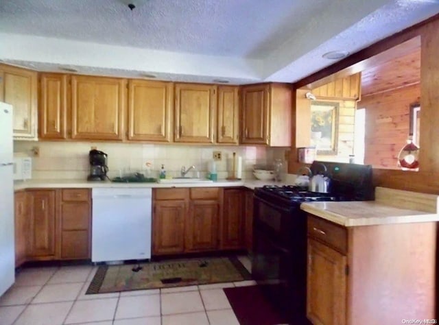 kitchen featuring dishwasher, sink, black gas range oven, wooden walls, and light tile patterned flooring