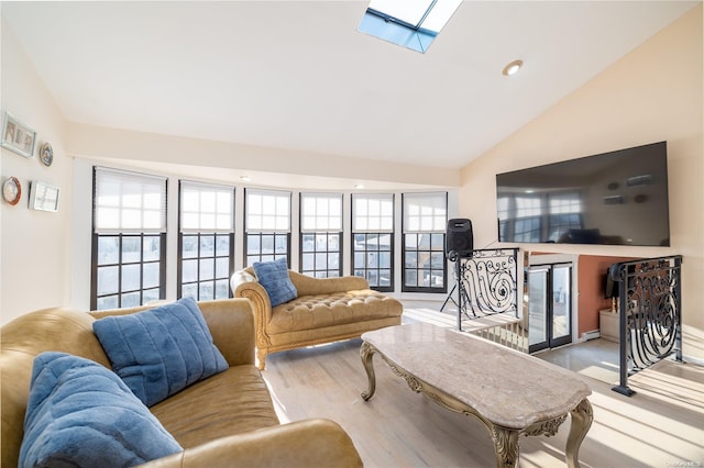 living room with light hardwood / wood-style floors, high vaulted ceiling, and a skylight