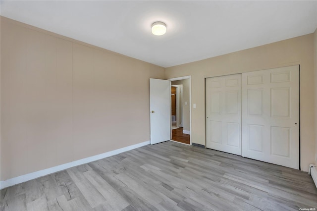 unfurnished bedroom with light hardwood / wood-style flooring, a closet, and a baseboard heating unit