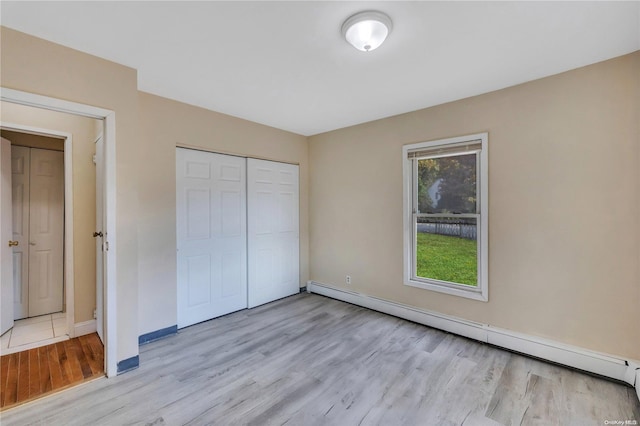 unfurnished bedroom with a closet, light hardwood / wood-style flooring, and baseboard heating