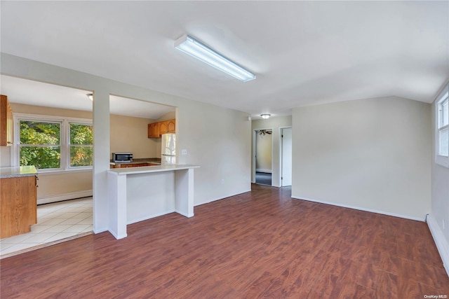 unfurnished living room with vaulted ceiling, light hardwood / wood-style flooring, and a baseboard heating unit