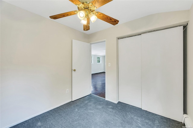 unfurnished bedroom with dark colored carpet, a closet, a baseboard radiator, and ceiling fan