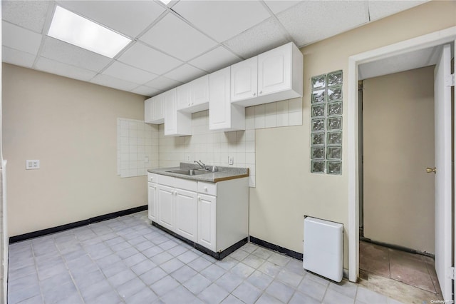 kitchen featuring white cabinets, decorative backsplash, a drop ceiling, and sink