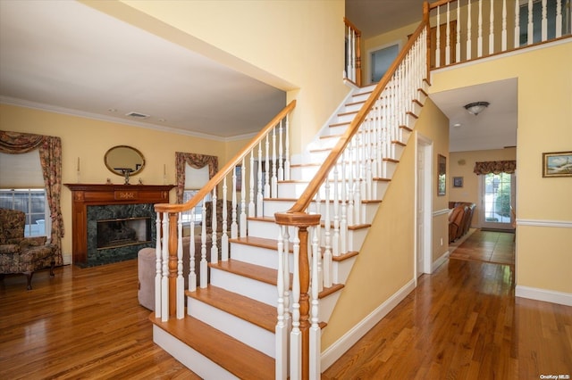 stairway featuring crown molding, a high end fireplace, and wood-type flooring