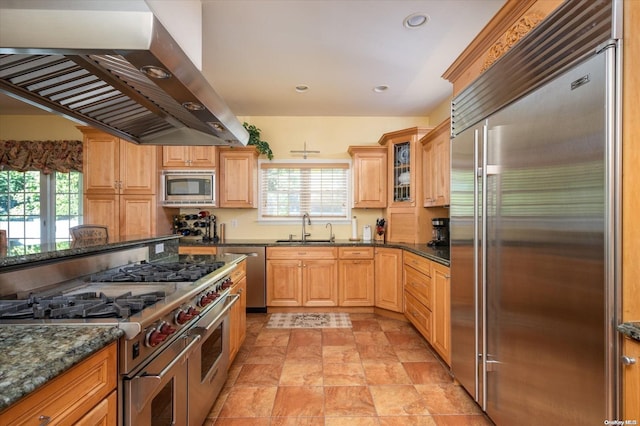 kitchen featuring sink, built in appliances, dark stone countertops, and wall chimney range hood