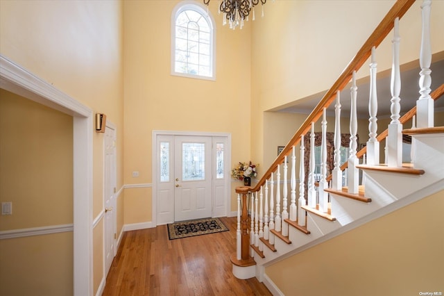 entryway with a towering ceiling, wood-type flooring, and an inviting chandelier