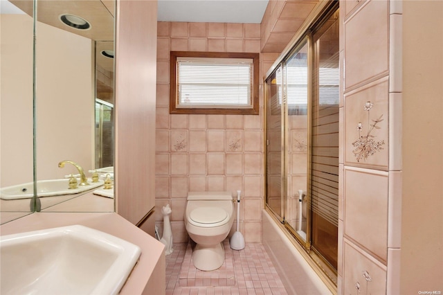 full bathroom with tile patterned floors, sink, bath / shower combo with glass door, toilet, and tile walls