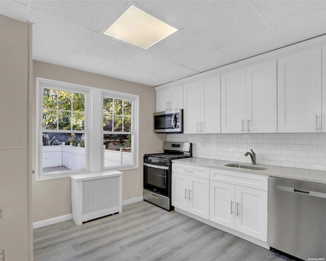 kitchen featuring radiator, white cabinets, sink, light wood-type flooring, and stainless steel appliances