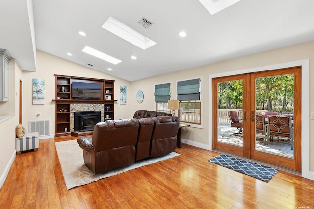 living room with vaulted ceiling with skylight, light hardwood / wood-style floors, and french doors