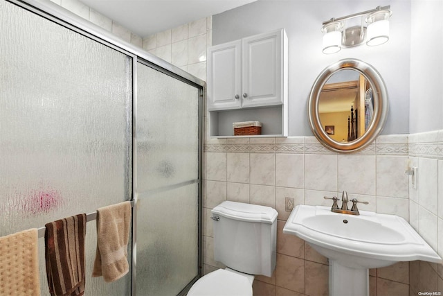 bathroom featuring sink, toilet, a shower with door, and tile walls