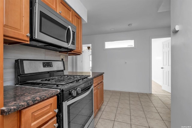 kitchen with backsplash, dark stone counters, ceiling fan, light tile patterned floors, and stainless steel appliances