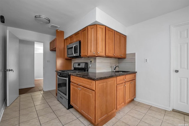 kitchen featuring backsplash, dark stone counters, sink, light tile patterned floors, and appliances with stainless steel finishes