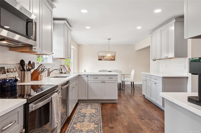 kitchen with appliances with stainless steel finishes, sink, gray cabinets, dark hardwood / wood-style floors, and hanging light fixtures