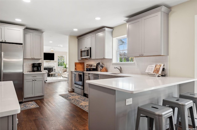 kitchen with a kitchen breakfast bar, dark hardwood / wood-style floors, backsplash, kitchen peninsula, and appliances with stainless steel finishes