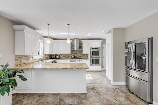 kitchen featuring kitchen peninsula, hanging light fixtures, wall chimney exhaust hood, white cabinetry, and stainless steel appliances