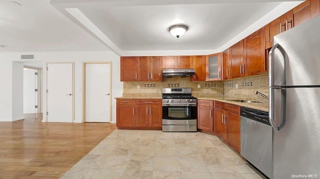 kitchen with appliances with stainless steel finishes, tasteful backsplash, light stone counters, sink, and light hardwood / wood-style floors