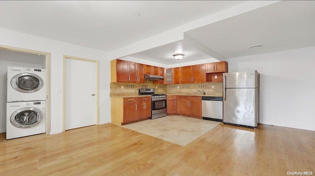 kitchen featuring backsplash, stainless steel appliances, stacked washer and clothes dryer, and light wood-type flooring