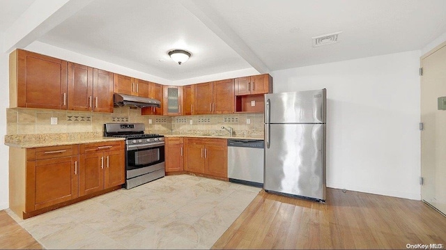 kitchen featuring light stone countertops, stainless steel appliances, tasteful backsplash, light hardwood / wood-style floors, and exhaust hood