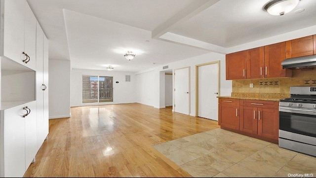 kitchen with light stone counters, light wood-type flooring, stainless steel range, and tasteful backsplash