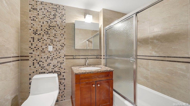 full bathroom featuring vanity, shower / bath combination with glass door, backsplash, toilet, and tile walls