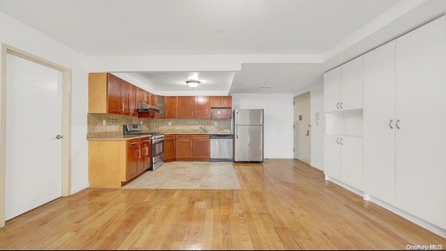 kitchen featuring exhaust hood, decorative backsplash, stainless steel appliances, and light wood-type flooring