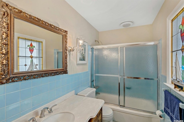 full bathroom featuring enclosed tub / shower combo, tile walls, vanity, and toilet