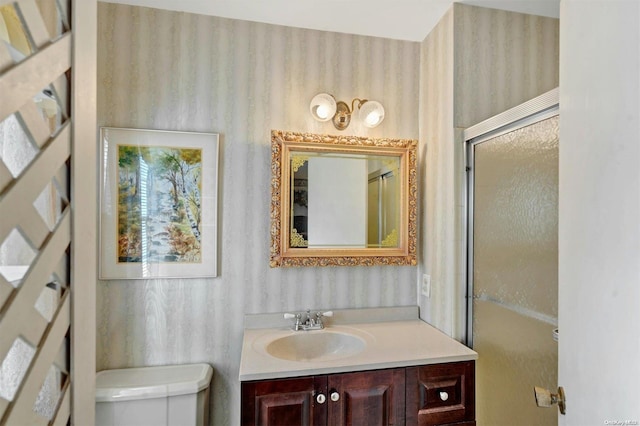 bathroom featuring a shower with door, vanity, and toilet