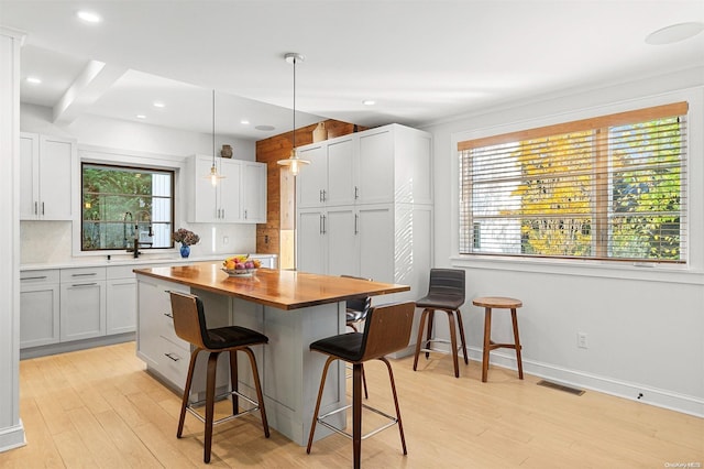 kitchen with white cabinetry, tasteful backsplash, pendant lighting, a breakfast bar area, and light wood-type flooring