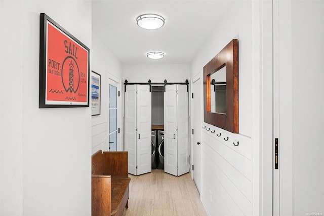 hallway with a barn door, washer and clothes dryer, and light wood-type flooring