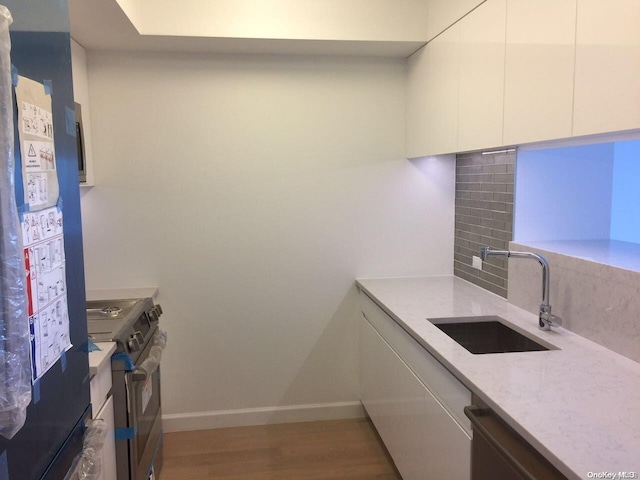 kitchen featuring backsplash, sink, appliances with stainless steel finishes, white cabinetry, and wood-type flooring