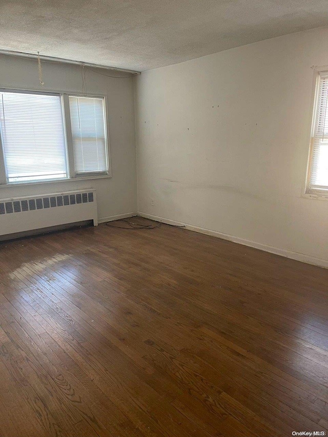 empty room with dark hardwood / wood-style flooring, radiator heating unit, and a textured ceiling