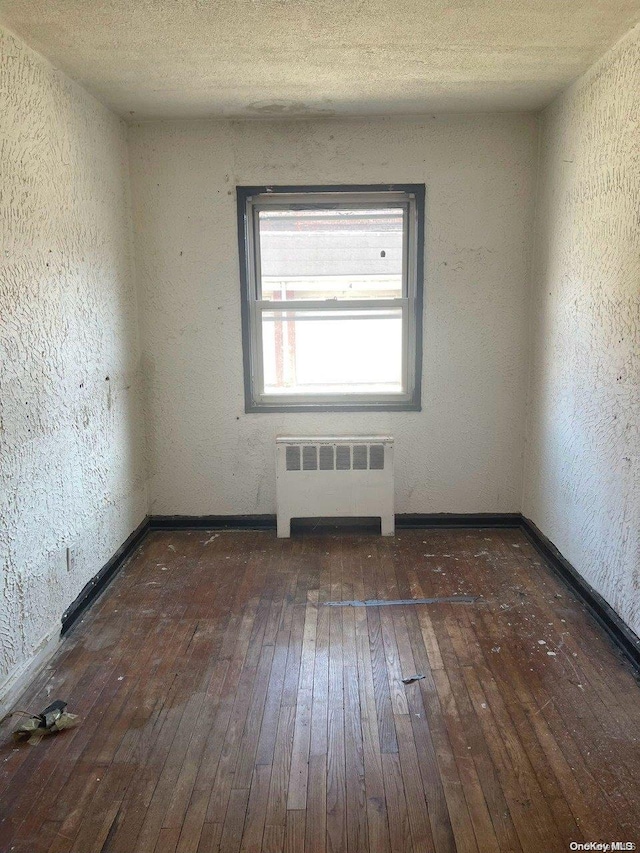 unfurnished room with a textured ceiling, radiator heating unit, and dark hardwood / wood-style floors