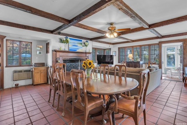 tiled dining room featuring ceiling fan, beamed ceiling, a healthy amount of sunlight, and a brick fireplace