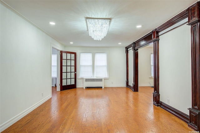 empty room featuring radiator heating unit, an inviting chandelier, and light wood-type flooring