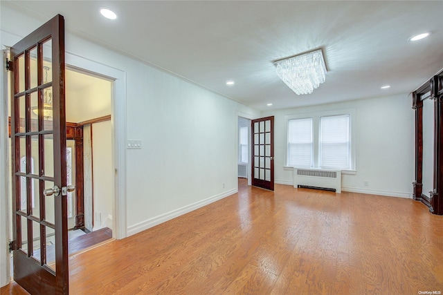 unfurnished room featuring a notable chandelier, light hardwood / wood-style floors, radiator heating unit, and french doors