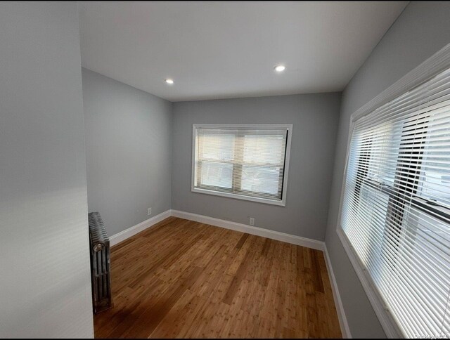 unfurnished room with hardwood / wood-style floors, radiator, and a healthy amount of sunlight