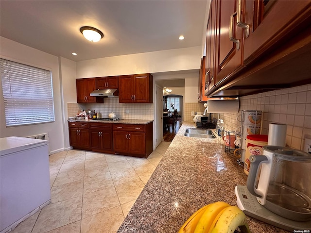 kitchen featuring stainless steel gas stovetop, backsplash, sink, dark stone countertops, and light tile patterned flooring