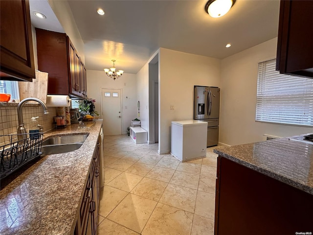 kitchen featuring backsplash, sink, decorative light fixtures, stainless steel fridge, and a notable chandelier