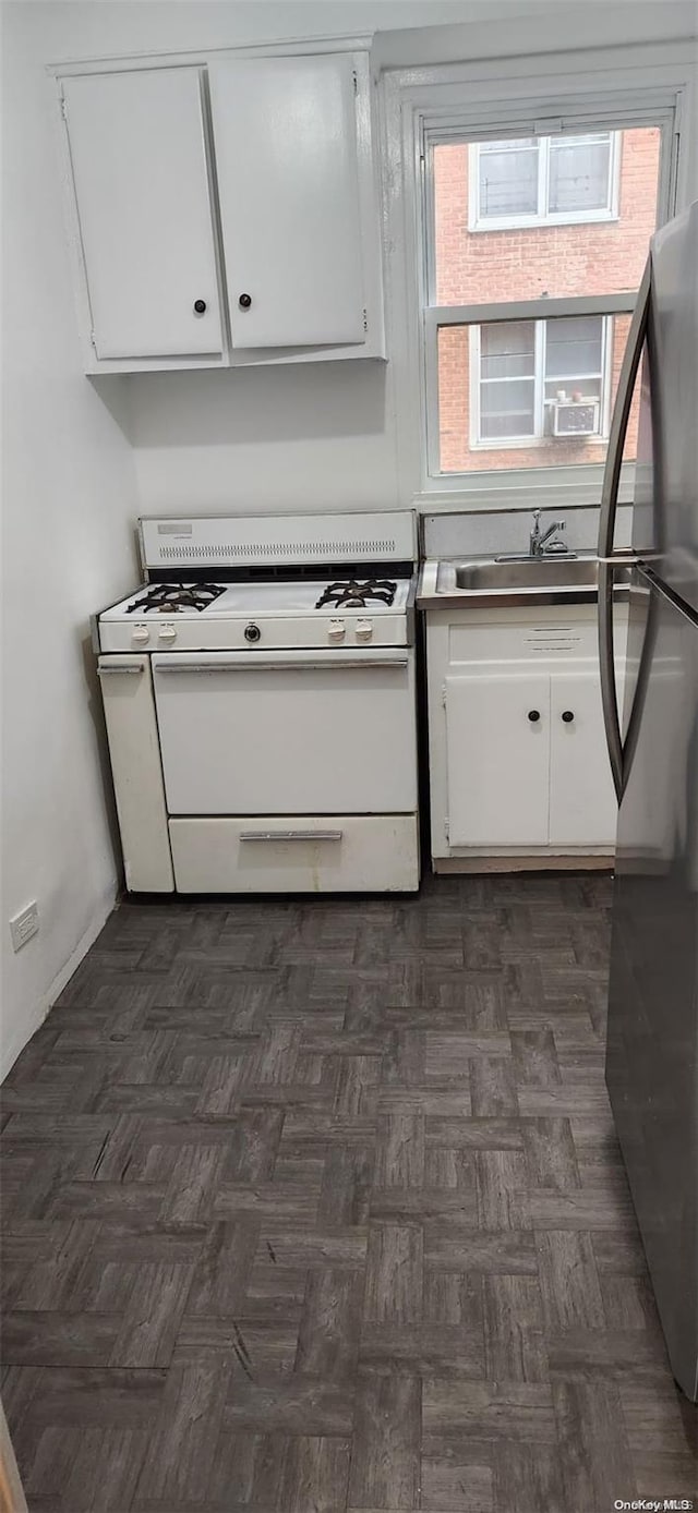 kitchen featuring sink, dark parquet floors, stainless steel fridge, white range with gas cooktop, and white cabinets